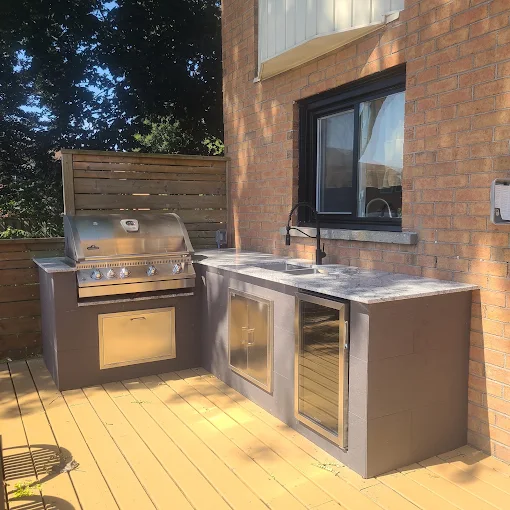 Built-in outdoor BBQ station with stone counter and bar fridge on a cedar deck